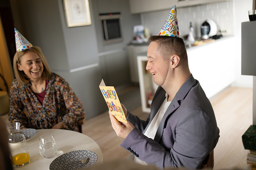 Happy man with special needs reading a Birthday card while having a party with his friend at home.