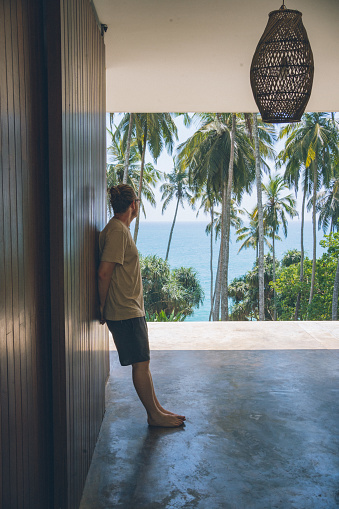 Young man looks toward sea and palm trees from porch