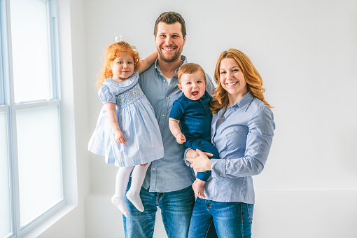 A young beautiful family couple with baby boy and 2 years daughter on gray studio
