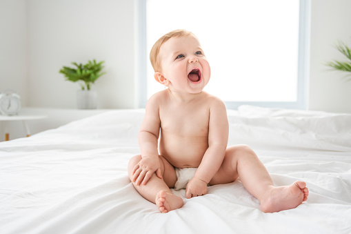 A Baby boy in diaper on white sunny bedroom. one years child relaxing in bed.