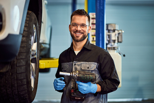 A smiling mechanic working in the repair shop service, holding a drill.