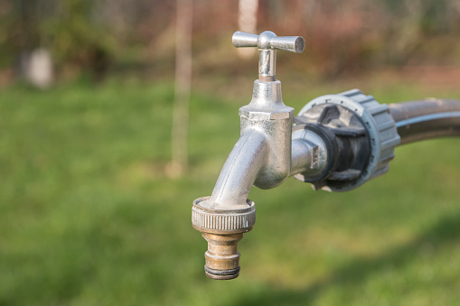 Water tap with metal garden hose adapter closeup on green grass background