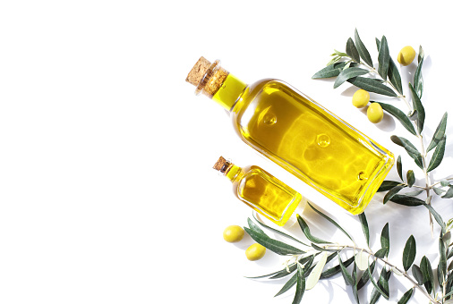 Two glass bottles of olive oil and sprigs of olive tree are on a white background. View from the top point. Copy space.