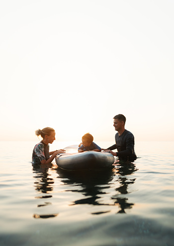 Photo of a young boy trying out to hold a balance on a paddle board for the first time. His parents are beside him, giving him support.