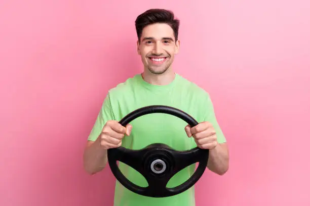Photo of cheerful handsome young guy driving steering wheel enjoying comfort volkswagen ag automobile isolated on pink color background.