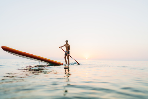 Photo of a young boy while paddleboarding the sea at sunset