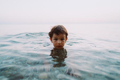 Photo of a young boy bathing and swimming in a refreshing salty sea water at sunset