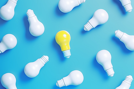 Lightbulbs on blue background. One of the lightbulbs is yellow colored. Horizontal composition.