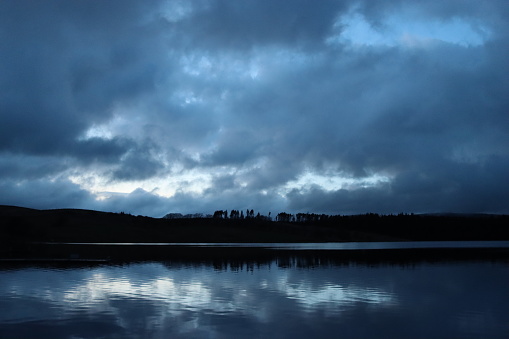 Dusk over a lake surrounded by trees, with dark storm clouds