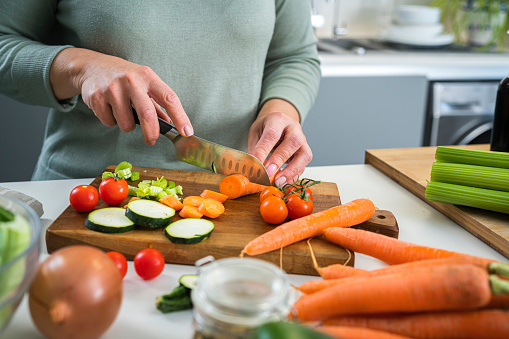 Close up of woman's hands slicing fresh organic carrots on kitchen counter