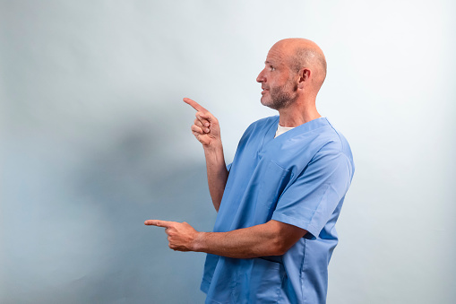 Portrait of a physiotherapist in light blue gown pointing at a side.