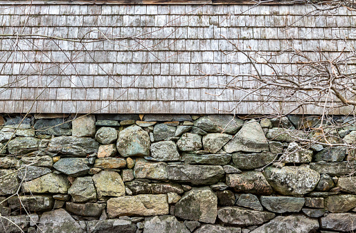 A close-up of a 18th century American colonial building exterior with a natural rock foundation wall and a wood shingle wall above.