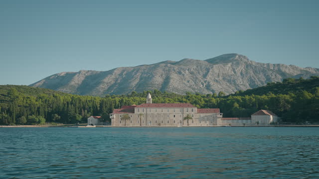 The view of Franciscan monastery from the blue sea on a sunny summer day. Visiting Badija island in Korcula. Beautiful mountains in the background.