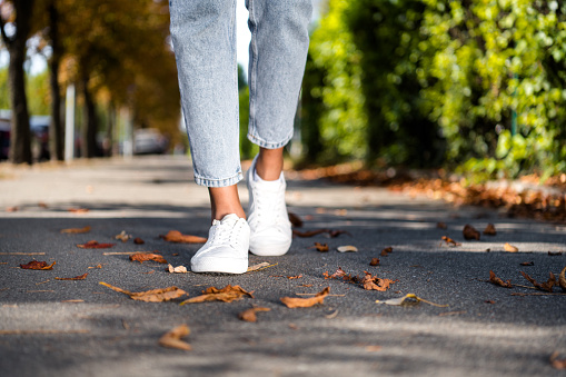 Cropped photo of female legs in white trendy sneakers going on shopping asphalt pavement.
