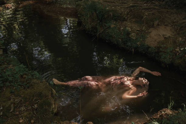 Serenely wearing a long pink dress lounges in the freshwater amidst a natural forest environment with verdant surroundings.