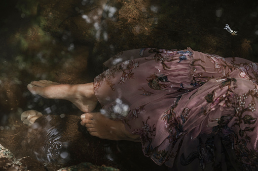 Woman cooling her feet in the water of a stream and wetting her dress.