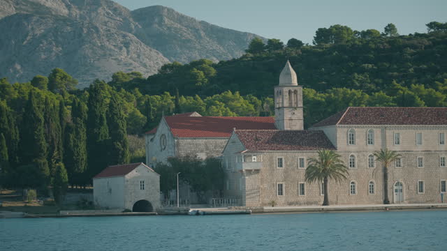 Beautiful Franciscan monastery in Korcula, Croatia. Monastery by the bright blue sea with mountains in the background.