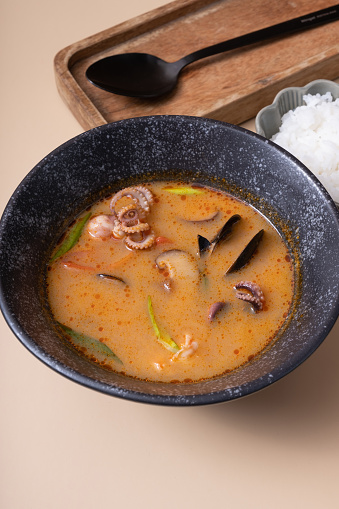 Tom yum soup and rice on a beige background angle view.
