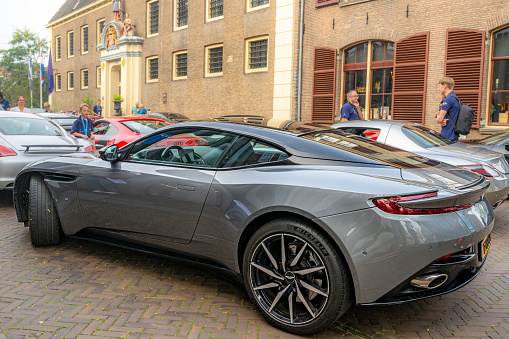 Aston Martin DB11 sports car in grey in the streets of Zwolle with people looking at the car. The Aston Martin DB11 is a luxury grand tourer unveiled in 2016 and available with V8 and V12 petrol engines.