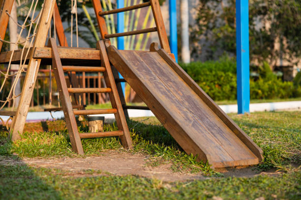 a playground in a tropical park with children's wooden slide and wooden stairs on the grass. evening light. - formal garden tropical climate park plant imagens e fotografias de stock