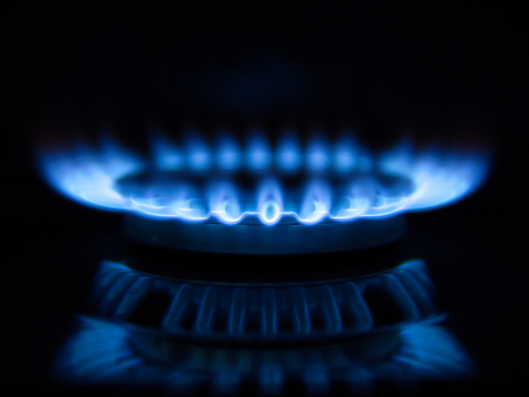 Macro closeup of modern luxury gas stove top with blue fire flame knobs and stainless steel pot with reflection and bokeh blurry blurred background