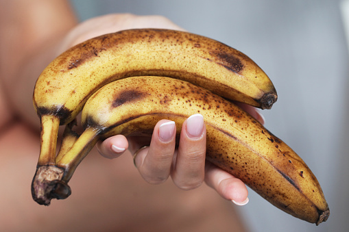 Healthy smoothie preparation. Rotten brown bananas. Woman hand holding fruits.