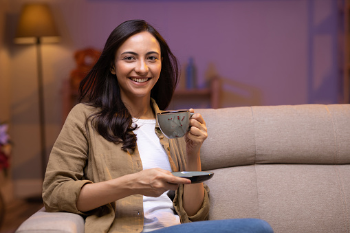 Young woman drinking tea sitting on sofa at home