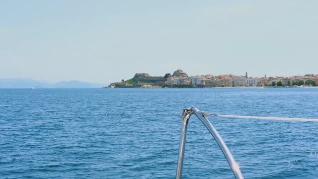 sailing by Corfu old city Kerkira in Greece, view from catamaran deck, colorful buildings, speed movement, waves, wind, fortress view