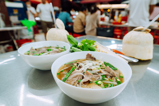 Two bowls of traditional Vietnamese Pho with fresh herbs in a busy street food market in Saigon, capturing the essence of local cuisine.