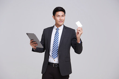 Happy smiling handsome Asian businessman in suit showing, presenting credit card for online payment isolated on white background.