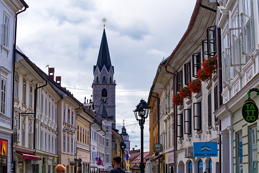 Old town of Slovenian City of Kranj with facades of historic houses and church tower with pedestrians and shops on a cloudy summer day. Photo taken August 10th, 2023, Kranj, Slovenia.