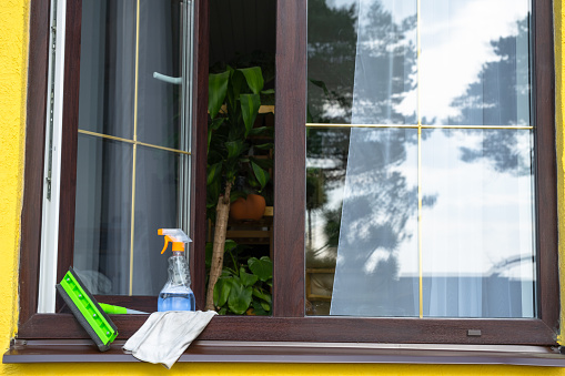 A window cleaning spray, a rag and a mop stand on the window sill of an open window outside for spring general cleaning