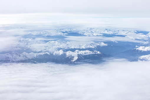 Snow covered mountains view through the clouds from above