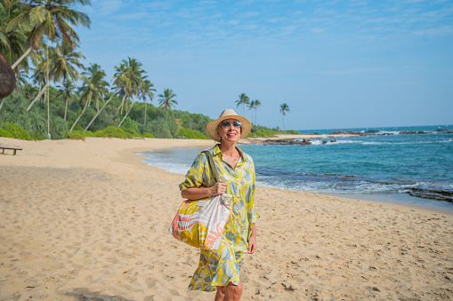 Mature woman walks down beach in sunhat