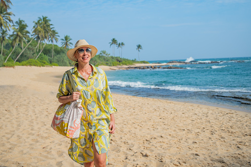 Mature woman walks down beach in sunhat