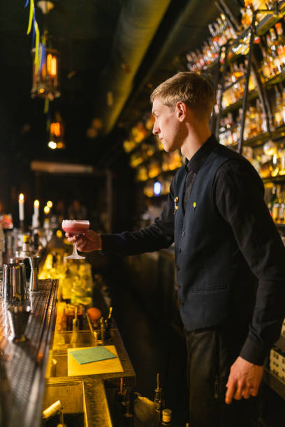 istock Young barkeeper serves delicious pink cocktail by counter 2094117881