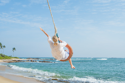Young woman swings over beach and sea