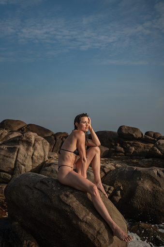 Young woman relaxes on rocky shoreline at dusk
