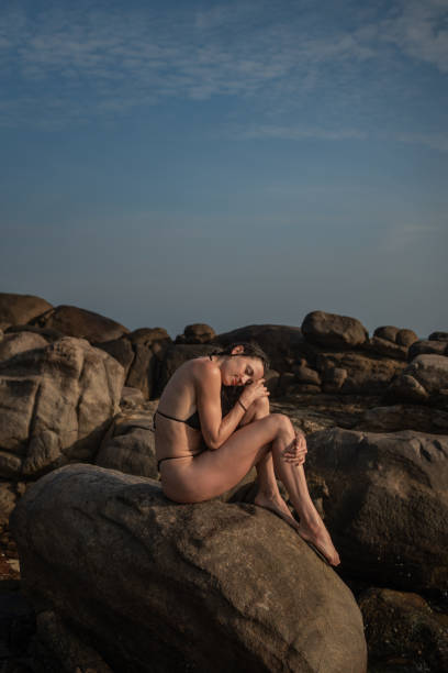 Young woman relaxes on rocky shoreline at dusk