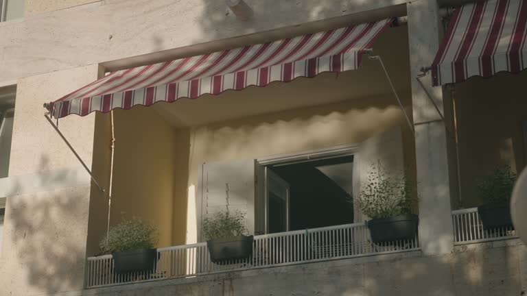 Terrace in the mediterranean village. Vacation balcony in the summer. White wodden shutters and flowers. Sun is creating shadows across the fasade.