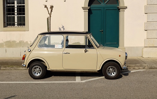 Percoto, Italy. March 17, 2024. Vintage beige Mini Cooper of the Seventies at the roadside. Side view.