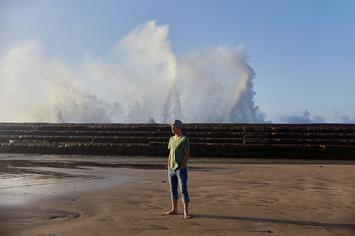 Solitary man watches as powerful waves break along a coastal pier under a clear sky. Tenerife, Spain
