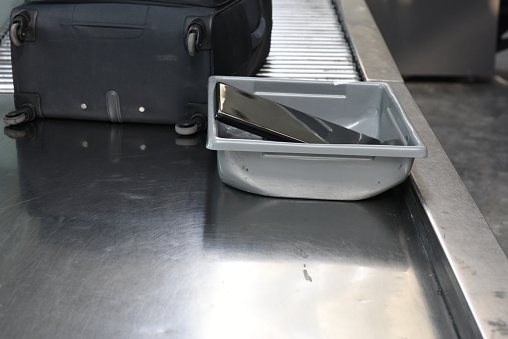 A tablet device in a security tray, moving along the conveyor belt for screening at an airport.