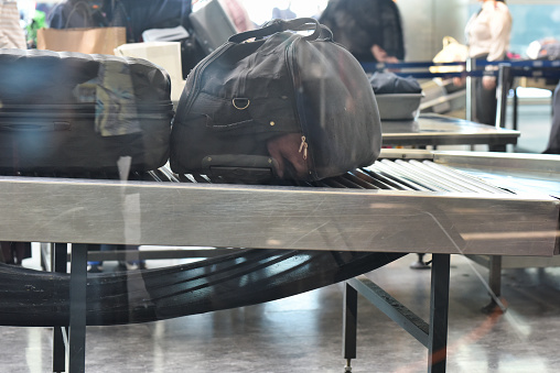 Bags and a duffel on an airport security conveyor belt, awaiting their turn through the X-ray scanner.