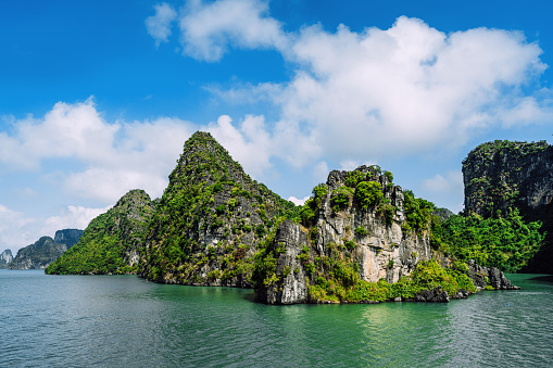 Scenic view of the iconic limestone karsts rising from emerald waters in Halong Bay, Vietnam, under a blue sky with clouds.