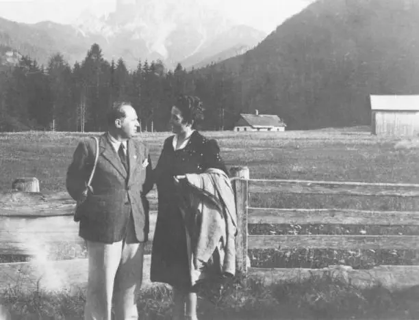 Mature couple standing in front of European Alps, Italy. 1952.