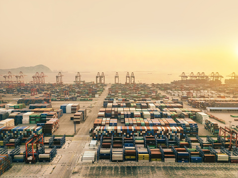 Golden sunset illuminates Shanghai Yangshan deepwater port, showcasing the expansive containers and shipping infrastructure from an aerial perspective.