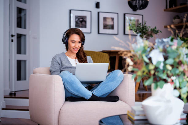 istock Full length of mid aged woman with headphone using a notebook at home 2094298083