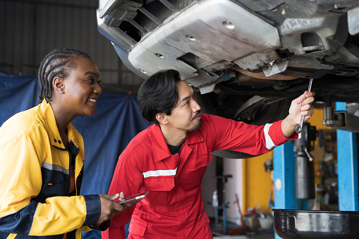 Male and female mechanic working at garage. Professional mechanics checks, repair and maintenance underneath lifted car at auto car repair service. Car service and Maintenance concept