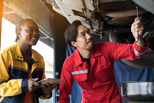 Male and female mechanic working at garage. Professional mechanics checks, repair and maintenance underneath lifted car at auto car repair service. Car service and Maintenance concept